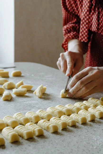 Hände schneiden Gnocchi-Teig in Reihen auf bemehlter Arbeitsfläche