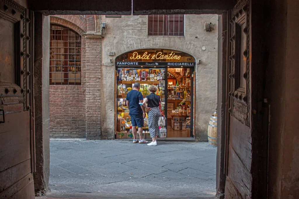 Boutique d'épicerie 'Dolci e Cantine' encadrée par une porte, couple regardant.