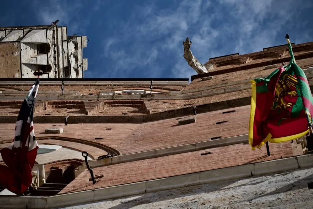 Drapeaux colorés accrochés à la façade gothique siennoise, vue en contreplongée
