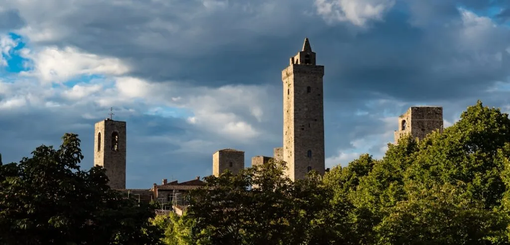 Tours médiévales de San Gimignano émergent derrière des arbres sous ciel orageux