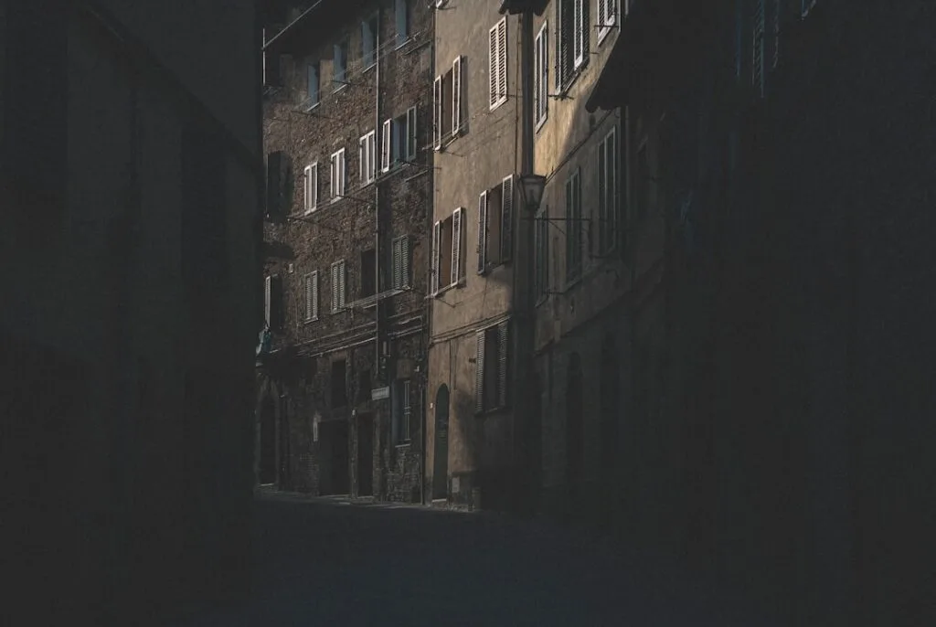 Dunkle, enge Gasse mit alten Häusern und Fensterläden in Siena
