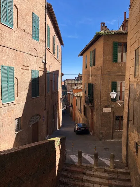rue en pente bordée d'immeubles en brique à Sienne, volets verts