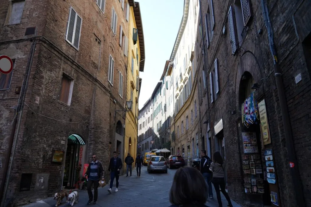 Ruelle étroite de Sienne bordée de bâtiments en brique et passants