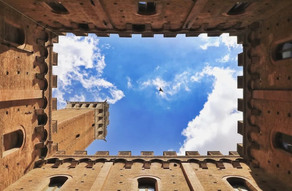 Vue verticale sur la Torre del Mangia entourée de murs à Sienne