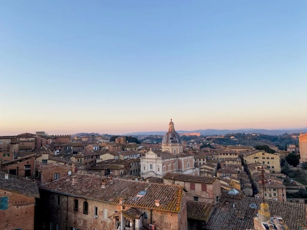 Uitzicht over terracotta daken en koepel van Siena bij schemer