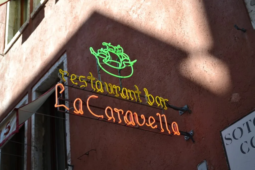 Enseigne néon « La Caravella » suspendue dans une ruelle de Sienne